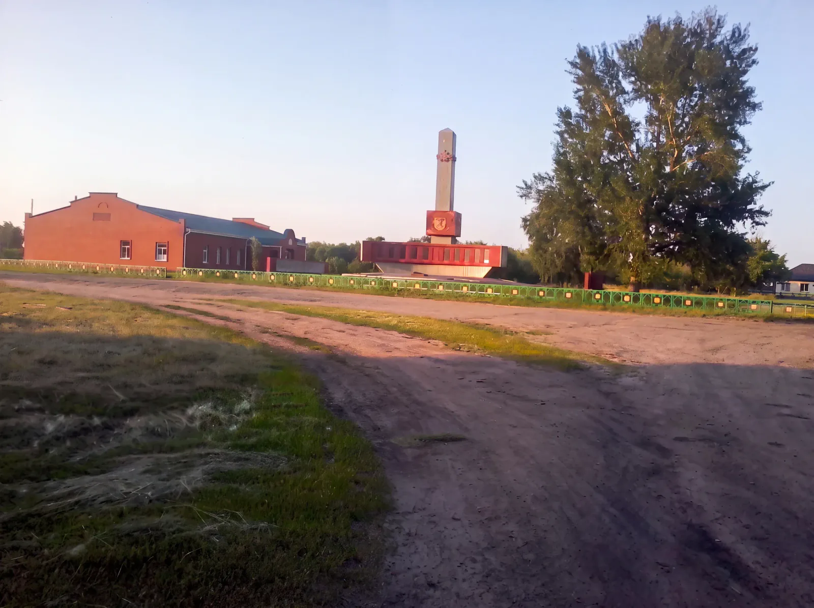 Центр села: кирпичное здание, мемориал с обелиском и высокие тополя