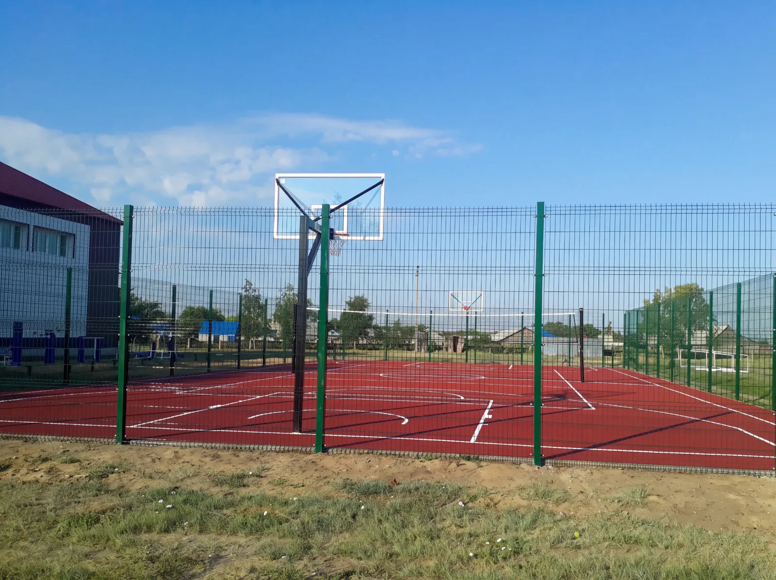 Новая спортивно-игровая площадка: резиновое покрытие, баскетбольное кольцо, ограждение, рядом спортзал школы