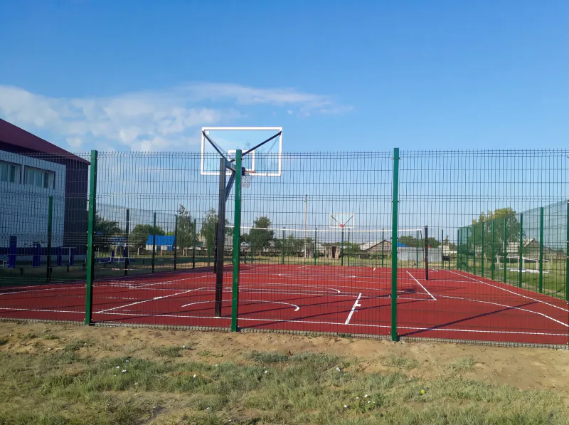 Новая спортивно-игровая площадка: резиновое покрытие, баскетбольное кольцо, ограждение, рядом спортзал школы
